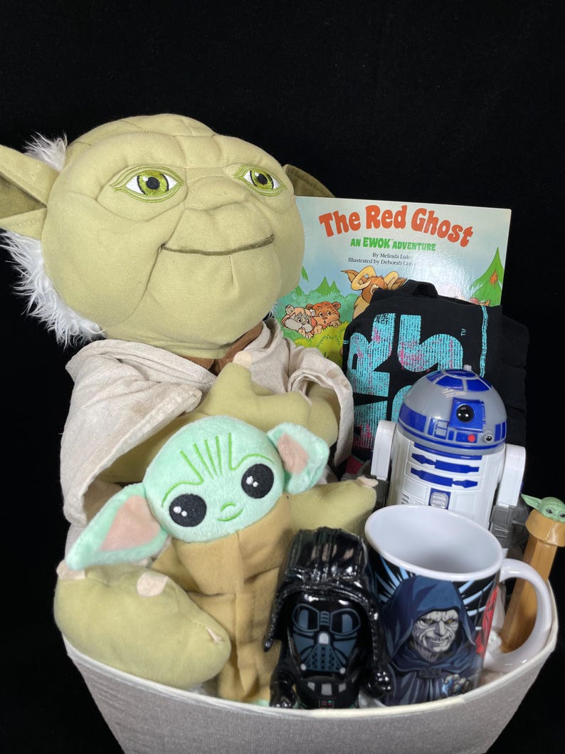 Op de afbeelding: Een Star Wars-thema cadeaupakket gevuld met een Yoda-knuffel, een Baby Yoda-knuffel, een Darth Vader-beeldje, een R2-D2-speelgoed, een mok met een karakterprint, een kinderboek getiteld "The Red Ghost" en een zwart t-shirt.