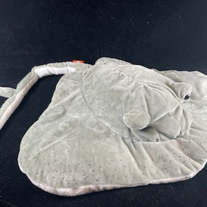 以下が含まれることがあります： 長い細い尾を持つ灰色のぬいぐるみエイ。エイは表面がざらざらしていて、白い下側があります。