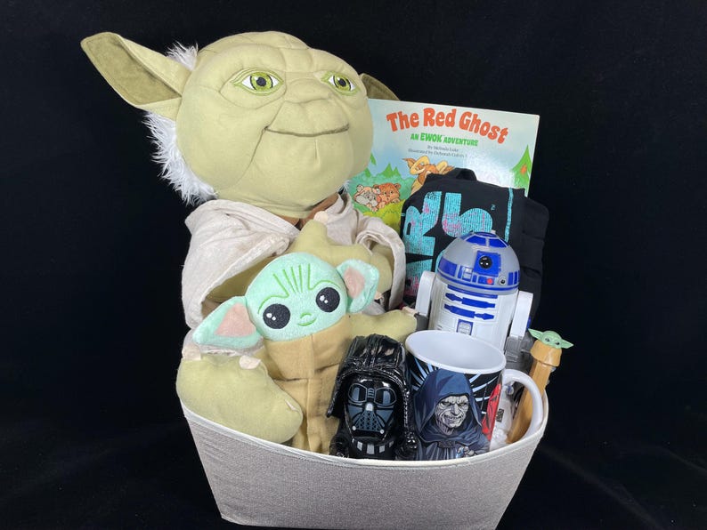 Op de afbeelding: Een grijze mand gevuld met Star Wars-items. Inclusief een groot Yoda-knuffel, een Baby Yoda-knuffel, een boek getiteld "The Red Ghost", een zwart t-shirt, een R2-D2-figuur, een mok en een Darth Vader-figuur.