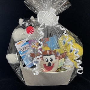 May include: A gift basket containing Looney Tunes character plush toys, such as Sylvester, Tweety Pie, and Taz. The basket is wrapped in clear cellophane and tied with a white bow. A Hot Wheels Looney Tunes car is also included.