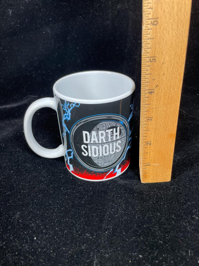Op de afbeelding: Witte keramische mok met een zwarte achtergrond met de tekst "Darth Sidious" in een witte ovaal. De mok heeft een wit handvat en een rood en blauw bliksemontwerp. De mok is ongeveer 7,6 cm hoog.