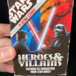 May include: Star Wars playing cards box featuring Luke Skywalker and Darth Vader with lightsabers. The box is labelled "Heroes & Villains" and states it features 55 characters from Star Wars.
