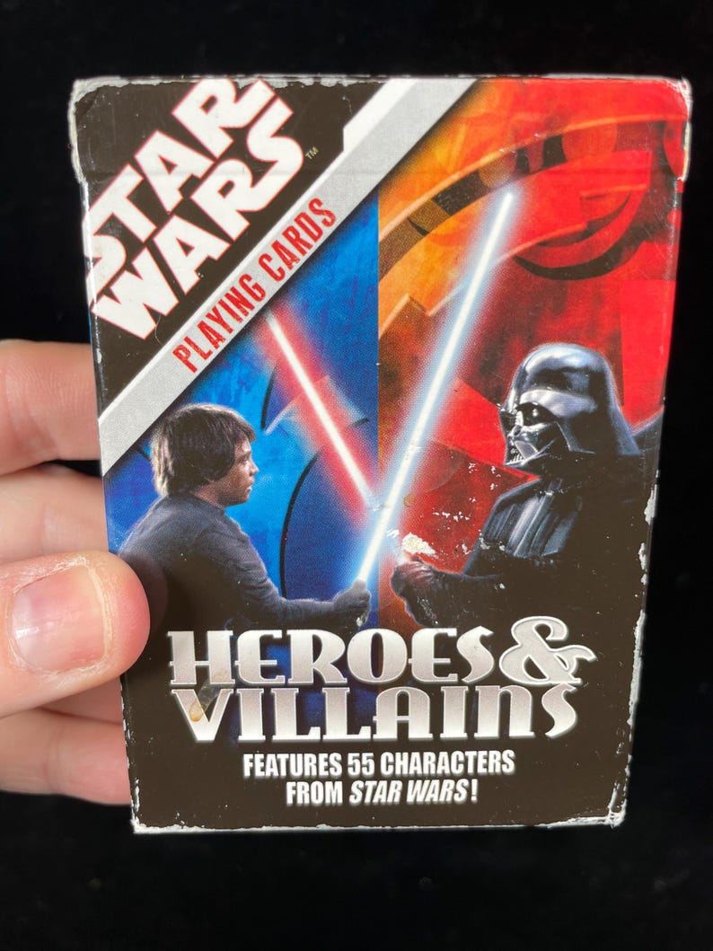 May include: Star Wars playing cards box featuring Luke Skywalker and Darth Vader with lightsabers. The box is labelled "Heroes & Villains" and states it features 55 characters from Star Wars.