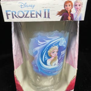 May include: A clear glass tumbler featuring Elsa from Disney's Frozen II, with the words "True to You". The tumbler is packaged in a cardboard box with the Frozen II logo and images of Anna and Elsa. The tumbler holds 16 oz (473 ml).