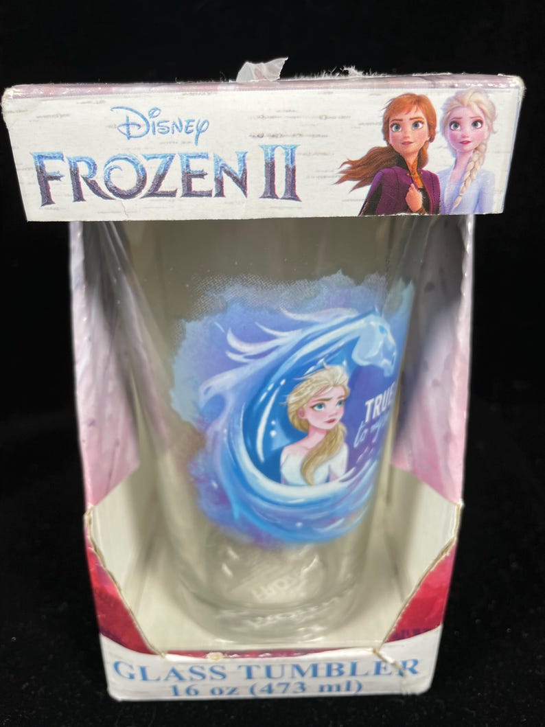 May include: A clear glass tumbler featuring Elsa from Disney's Frozen II, with the words "True to You". The tumbler is packaged in a cardboard box with the Frozen II logo and images of Anna and Elsa. The tumbler holds 16 oz (473 ml).
