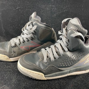 May include: A pair of black high-top sneakers with gray laces and a white sole. The sneakers have a perforated design on the side and a red stitching detail.