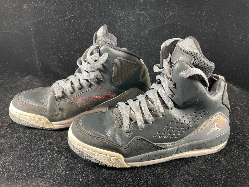 May include: A pair of black high-top sneakers with gray laces and a white sole. The sneakers have a perforated design on the side and a red stitching detail.