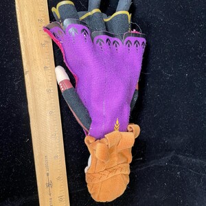 May include: A purple and black glove with gold trim, featuring a brown cuff and a decorative pattern. The glove is approximately 5 inches long, with a wooden ruler in the image for scale.