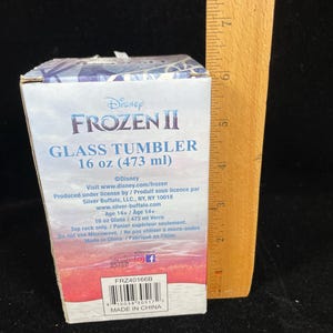 May include: A Disney Frozen II glass tumbler in a box. The box is white and blue with the Frozen II logo and text. The tumbler holds 16 oz (473 ml). The box also includes product information and a barcode.