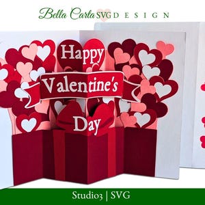 May include: A Valentine's Day pop-up card with a red gift box design. The card features layers of red, pink, and white hearts, with a banner that reads "Happy Valentine's Day." The card is white with red heart accents.