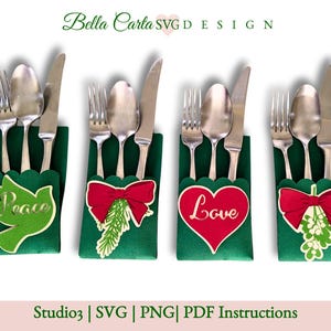 May include: Four green place card holders with a red bow and a Christmas-themed design. Each holder has a different design: a dove with the word "Peace", a sprig of holly with a red bow, a heart with the word "Love", and a sprig of mistletoe with a red bow. The holders are designed to hold a fork, knife, and spoon.