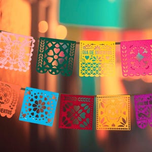 May include: A string of colorful paper banners with cut-out designs, including skulls, flowers, and the text "Dia de Muertos".