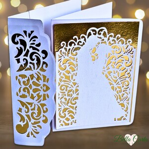 May include: A white and gold laser-cut wedding invitation card featuring an intricate filigree pattern on the front flap and a silhouette of a couple embracing on the main panel, set against a metallic gold background with a scalloped edge design.
