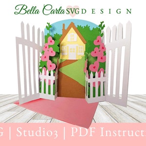 May include: A 3D paper craft pop-up card featuring a yellow house with a brown roof, a brown path, and green foliage. The scene is framed by white picket fences and pink heart-shaped flowers. Text at the top reads Bella Carta SVG DESIGN.