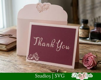 May include: A light pink envelope with a laser-cut rose design on the flap stands behind a folded card. The card features a dark maroon rectangular panel with the text "Thank You" in a light script font and a small rose cutout in the corner.