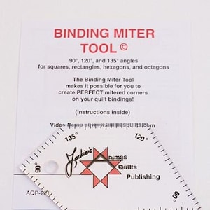 May include: A clear plastic tool for creating mitered corners on quilt bindings. The tool has markings for 90, 120, and 135 degree angles. The tool is labeled "Binding Miter Tool" and "Jackini's Nimas Quilts Publishing".
