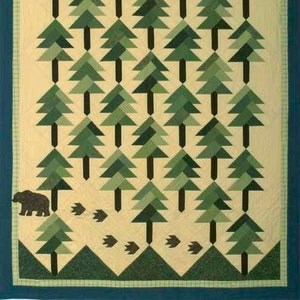 May include: A quilt with a beige background and a pattern of green trees. The trees are made of triangles and are arranged in rows. A black bear is walking across the bottom of the quilt.