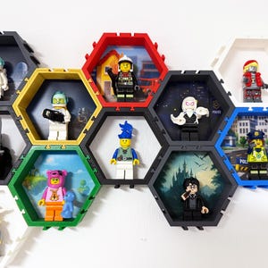Könnte beinhalten: Eine Sammlung von Lego-Minifiguren, die in farbenfrohen, sechseckigen Wandregalen ausgestellt sind. Die Figuren repräsentieren verschiedene Themen, darunter Astronauten, Feuerwehrleute und Charaktere mit Gitarren. Die Regale sind an einer weißen Wand montiert.