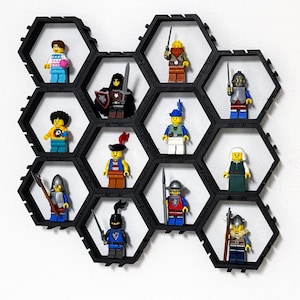 Könnte beinhalten: Ein schwarzes sechseckiges Display-Regal mit mehreren Fächern, in denen jeweils eine Lego-Minifigur steht. Die Minifiguren sind in verschiedenen Outfits gekleidet, darunter Ritter, Soldaten und andere historische Charaktere. Das Regal ist an einer weißen Wand befestigt.