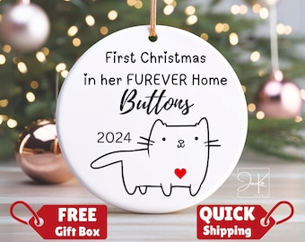 May include: White ceramic Christmas ornament with a black cat illustration and the text "First Christmas in her furever home Buttons 2024".