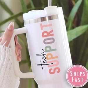 May include: White insulated tumbler with a handle, featuring the words "Tech Support" in colorful letters. The tumbler has a silver rim and a white lid. A pink and white sticker that says "Ships Fast" is on the bottom right.