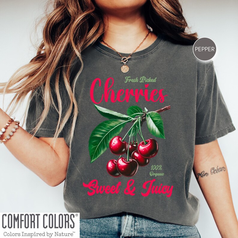 May include: A gray t-shirt with a graphic of red cherries on a green stem with leaves. The text "Fresh Picked Cherries" is above the cherries and "Sweet & Juicy" is below the cherries. The text "100% Organic" is to the right of the cherries.