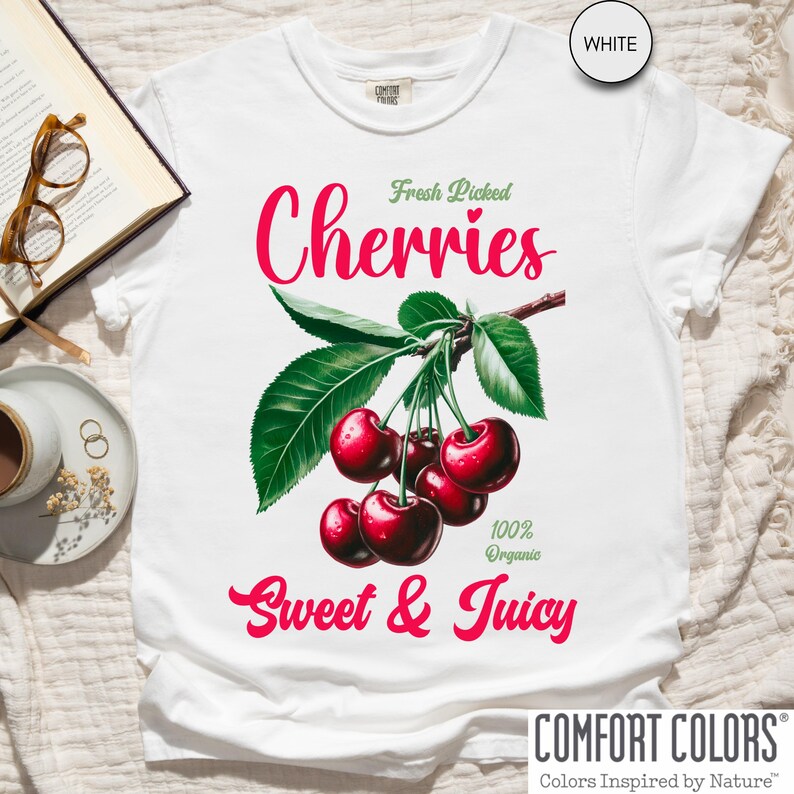 May include: White t-shirt with a graphic of red cherries on a branch with green leaves. The text "Fresh Picked Cherries" is above the cherries and "100% Organic Sweet & Juicy" is below the cherries.
