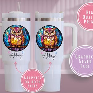 May include: White travel mug featuring a colorful owl design in a stained-glass style. The owl is perched on a branch within a circular frame. The name "Abbey" is written below the owl. The mug has a handle and a straw.