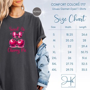 May include: A dark gray t-shirt with a pink cherry pie graphic and the text "Sweet as Cherry Pie". The shirt is a unisex garment-dyed t-shirt. A size chart is included with measurements in inches.