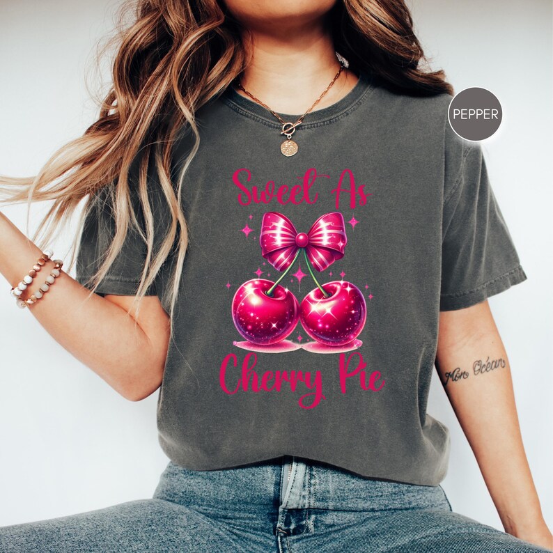May include: A dark gray t-shirt with a pink cherry pie graphic. The graphic features two cherries with a pink bow and the text "Sweet as Cherry Pie".