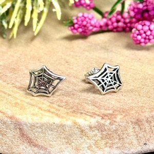 May include: A pair of silver spiderweb earrings. The earrings are small and delicate, and they feature a detailed spiderweb design.