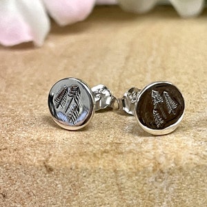 May include: A pair of silver stud earrings with a raised design of two pine trees on each earring.
