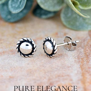 May include: A pair of silver stud earrings with a rope-like design around the edge of the circular face. The earrings have a slightly domed shape.