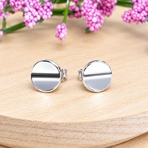 May include: A pair of polished silver-tone stud earrings featuring a simple, flat circular design. Each earring has a smooth, reflective surface and a standard post back, presenting a clean and uniform appearance for these small, circular jewelry pieces.