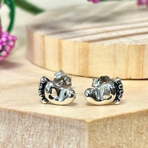 May include: A pair of silver baby foot earrings with a heart-shaped cutout in the center of each foot.