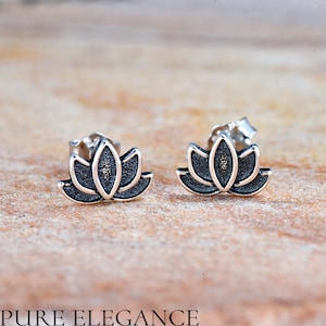 May include: A pair of silver lotus flower stud earrings. The earrings are small and delicate, with a black enamel finish.