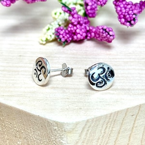 May include: A pair of silver stud earrings with a circular design featuring the Om symbol.