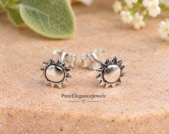 May include: A pair of silver-toned sun-shaped stud earrings with a textured finish and post backs. The text PureEleganceJewelz with a small heart symbol is printed below the earrings. The sun design features a smooth center and rays.