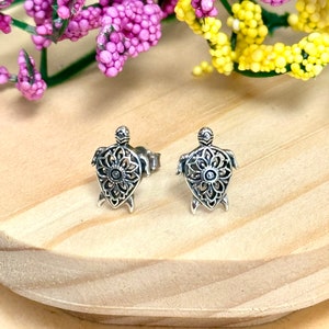 May include: A pair of silver turtle stud earrings with a delicate filigree design. The turtles have a circular pattern on their shells.