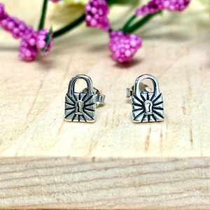 May include: A pair of silver lock and key stud earrings. The lock is detailed with a keyhole and a sunburst design.