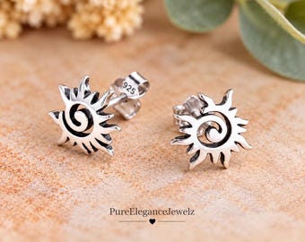 May include: A pair of sterling silver stud earrings shaped like stylized suns with a central spiral design. The earrings feature a polished finish with oxidized recessed areas and are stamped with 925 on the post. PureEleganceJewelz.
