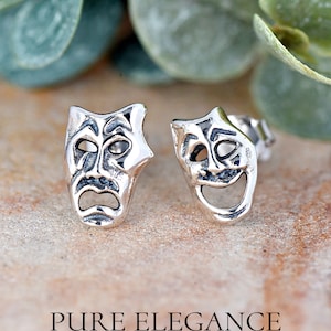 May include: A pair of silver earrings featuring a stylized design of a laughing and a crying mask. The masks are a classic symbol of theater and performance.