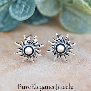 May include: A pair of silver sun stud earrings. Each earring features a detailed sun design with a round center.