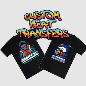 May include: Two black t-shirts with custom heat transfers. One shirt features a gorilla wearing a basketball jersey with the word "GORILLAS" below. The other shirt features a shark wearing a basketball jersey with the word "SHARKS" below. The text "CUSTOM HEAT TRANSFERS" is written in a colourful, graffiti-style font above the shirts.