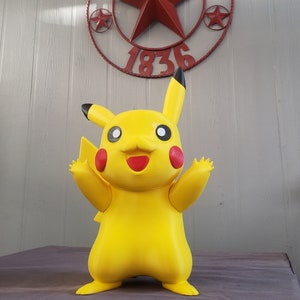 May include: A yellow Pikachu figurine with black ears and a red smile. The figurine is standing on a gray surface with a red metal star and the text "Texas 1836" in the background.