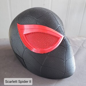 May include: Black and red 3D printed mask with a spider web design. The mask has a red eye piece with a mesh design.