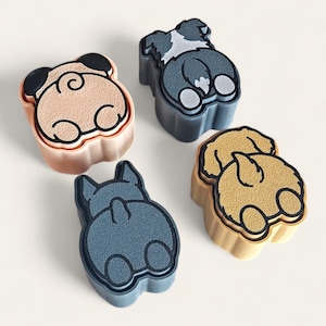 May include: Four dog-shaped molds in various colors: tan, light blue, and peach. Each mold features a different dog breed's rear end, outlined in black. The molds are arranged on a white surface.