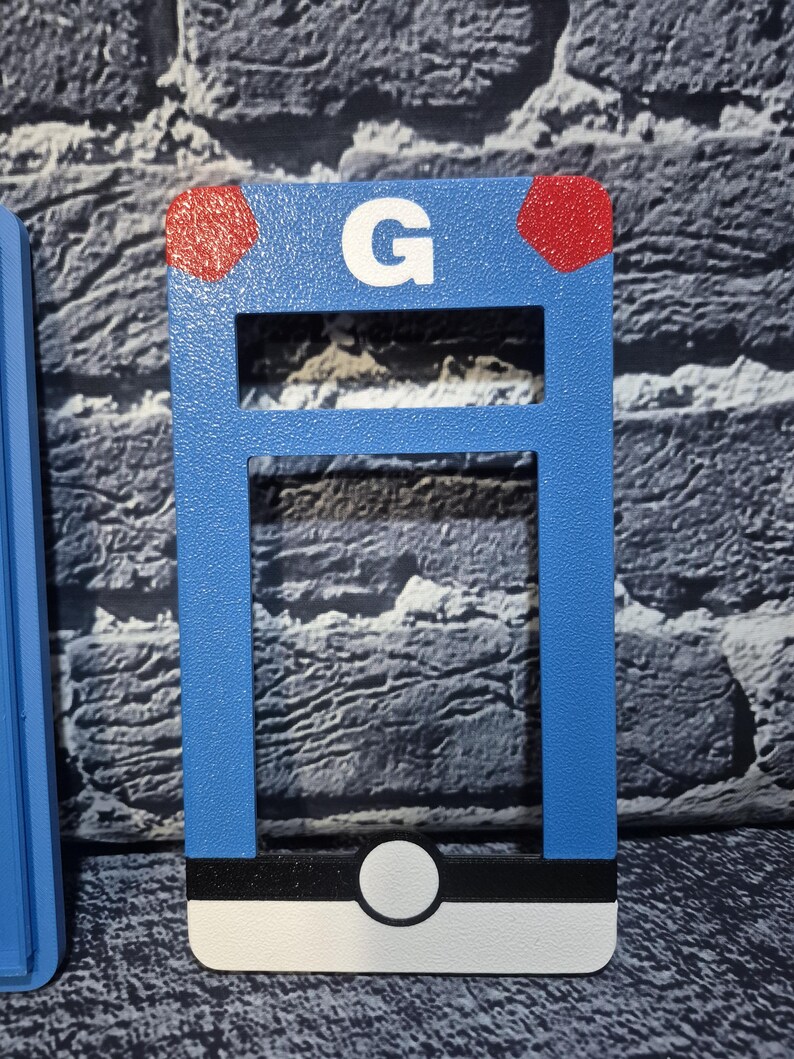 May include: A blue rectangular object with a white "G" and two red dots. The object has a white, black, and white design at the bottom. The object is a decorative item.