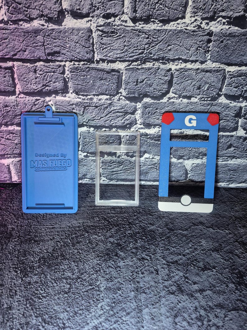 May include: Three 3D-printed objects: a blue clipboard with text, a clear rectangular frame, and a blue and white structure with a red accent and the letter "G". The objects are on a textured surface.