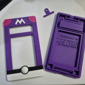 May include: A purple and white 3D-printed case, featuring a white "M" logo and a circular design. The case is designed to hold a device and has the text "Designed By MAS FUEGO 3D PRODUCTIONS".